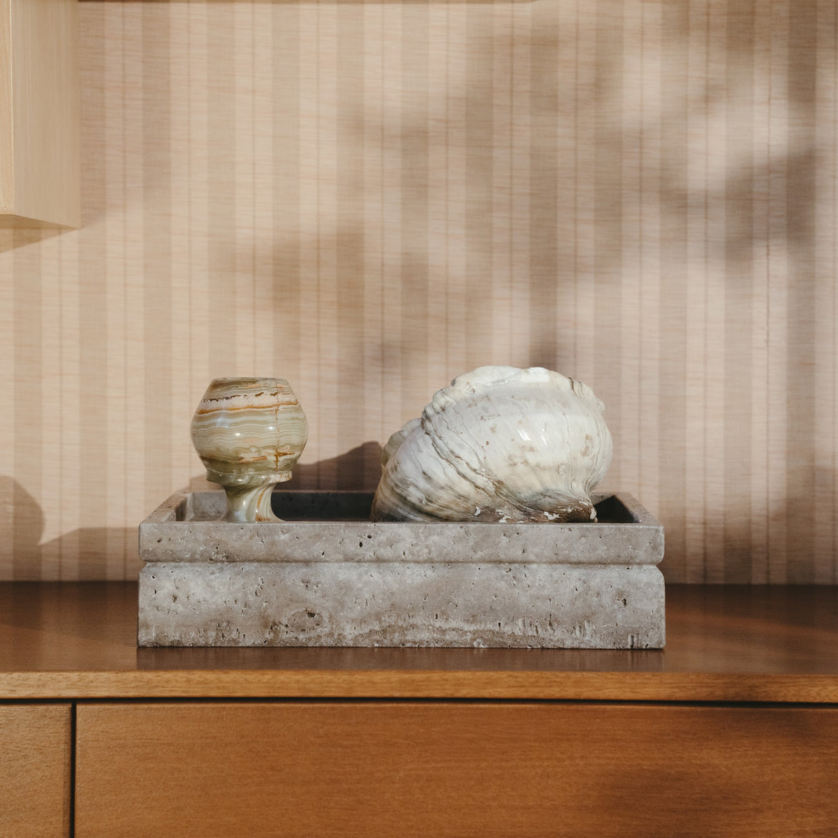 Silver travertine Tray urn resting quietly on a sideboard with a shell and a small vase
